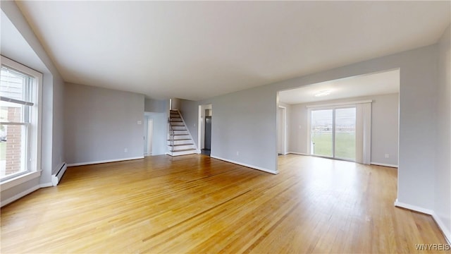unfurnished living room featuring light wood finished floors, stairway, a baseboard radiator, and baseboards