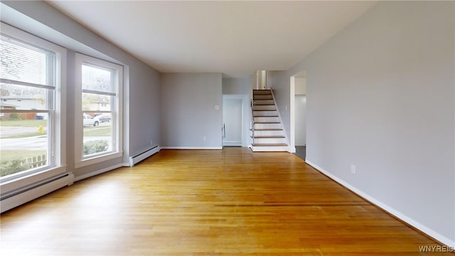 unfurnished living room featuring a baseboard heating unit, stairway, and light wood-type flooring