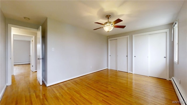 unfurnished bedroom with light wood-style flooring, baseboards, baseboard heating, multiple closets, and a baseboard radiator
