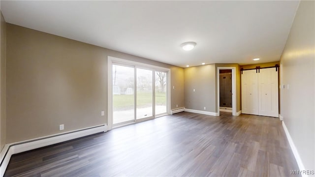 empty room with baseboards, a barn door, wood finished floors, and a baseboard heating unit