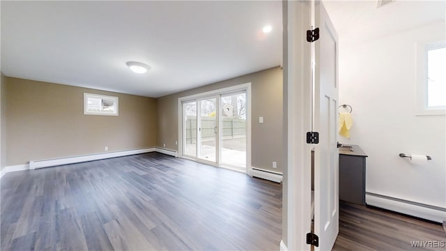 spare room featuring baseboards, a baseboard heating unit, and dark wood-type flooring