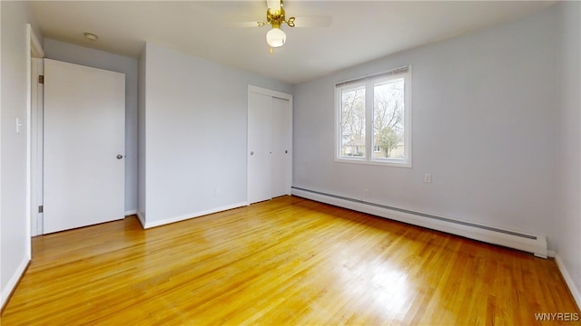 unfurnished bedroom with a closet, light wood-style flooring, baseboard heating, and baseboards