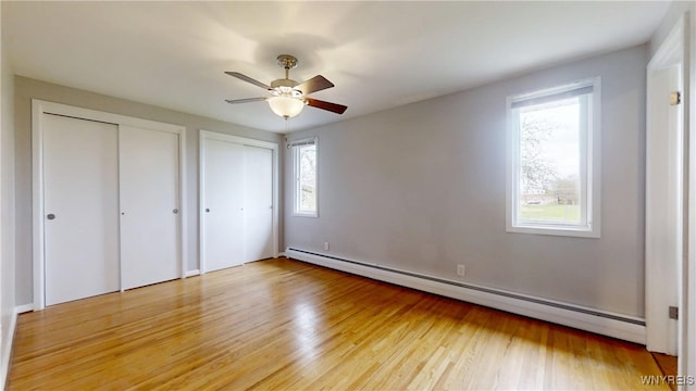 unfurnished bedroom with two closets, light wood-type flooring, a ceiling fan, and a baseboard heating unit