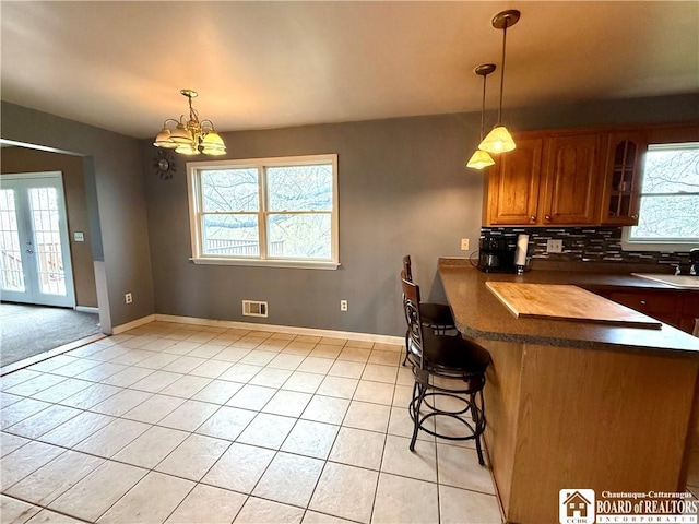 kitchen featuring brown cabinets, a breakfast bar, visible vents, dark countertops, and light tile patterned flooring