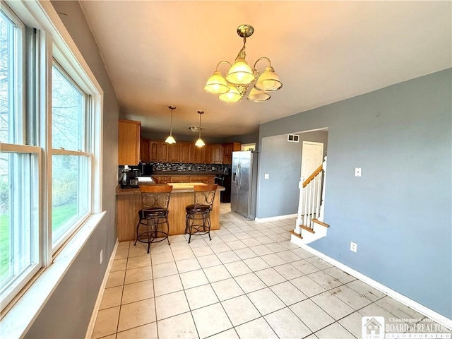 kitchen with light tile patterned floors, an inviting chandelier, stainless steel fridge with ice dispenser, a peninsula, and backsplash