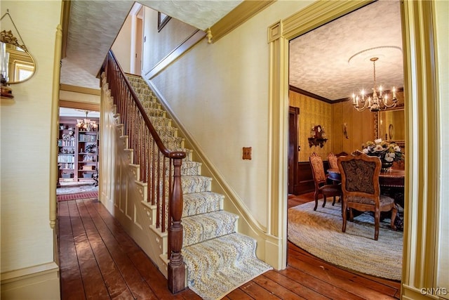 stairs with ornamental molding, an inviting chandelier, and hardwood / wood-style flooring