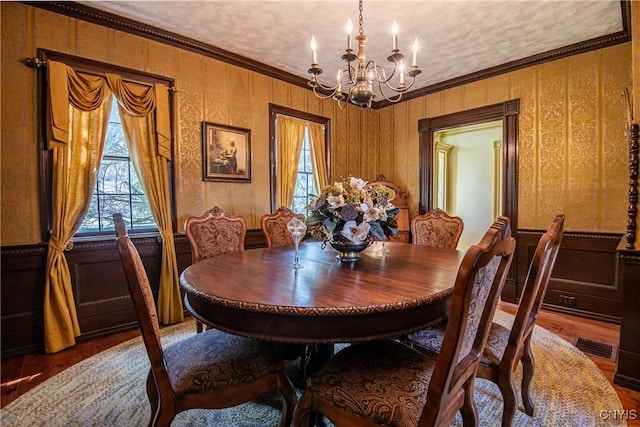 dining room featuring wood finished floors, a decorative wall, a chandelier, wainscoting, and ornamental molding