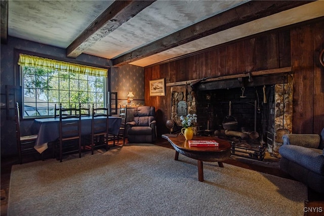 carpeted living room with wooden walls, a wood stove, and beam ceiling