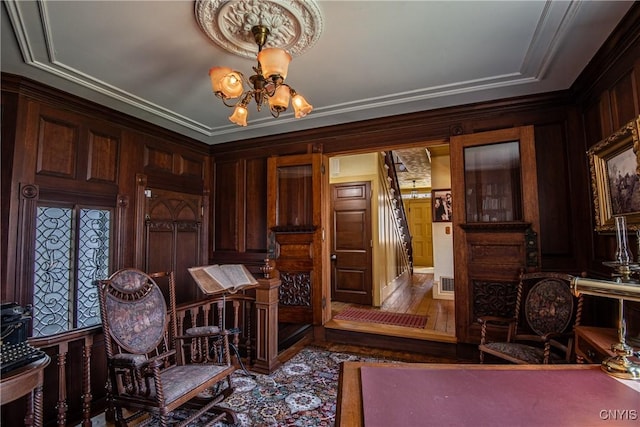 living area with crown molding, a notable chandelier, wood walls, and wood finished floors
