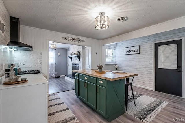 kitchen with wall chimney range hood, a textured ceiling, butcher block countertops, and green cabinets