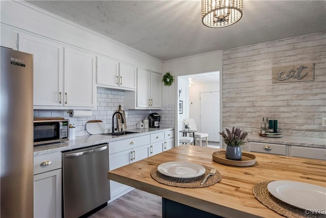 kitchen with a sink, butcher block countertops, stainless steel appliances, backsplash, and white cabinetry