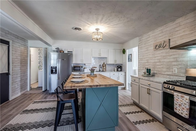 kitchen featuring a sink, a breakfast bar, wood walls, white cabinets, and appliances with stainless steel finishes