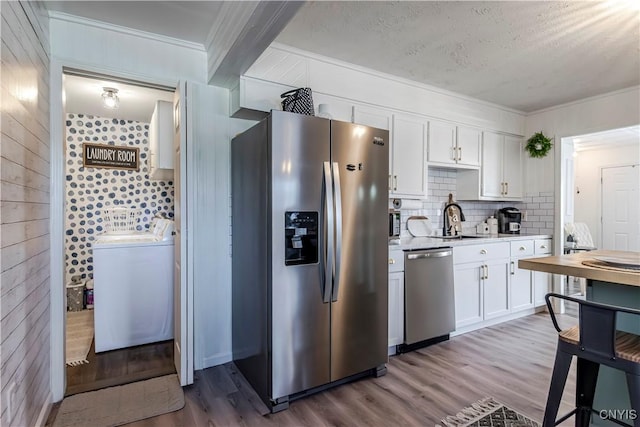 kitchen with crown molding, a sink, appliances with stainless steel finishes, and washer / dryer