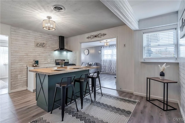 kitchen featuring wood finished floors, a breakfast bar, wood counters, wall chimney range hood, and stainless steel range oven