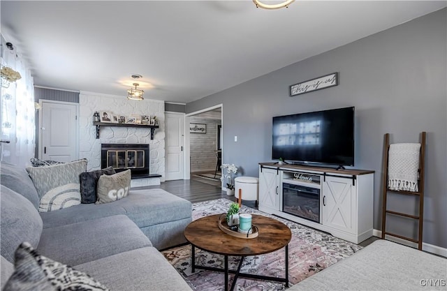 living area featuring wood finished floors, a stone fireplace, and baseboards