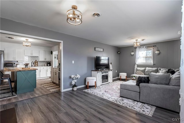 living room with a chandelier, visible vents, dark wood-style floors, and baseboards