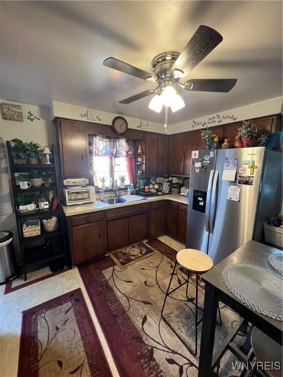 kitchen with dark brown cabinetry, stainless steel fridge with ice dispenser, light countertops, a sink, and a ceiling fan