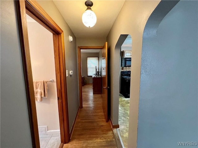 hallway featuring baseboards, visible vents, arched walkways, and light wood-style floors
