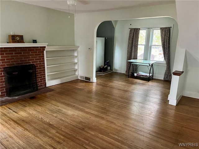 unfurnished living room with visible vents, baseboards, arched walkways, a fireplace, and wood finished floors