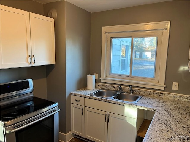 kitchen with electric stove, white cabinets, light stone counters, and a sink