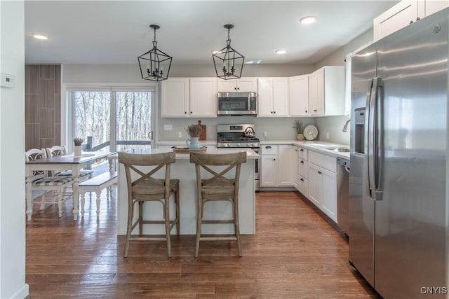 kitchen with appliances with stainless steel finishes, light countertops, white cabinets, dark wood-style floors, and a center island