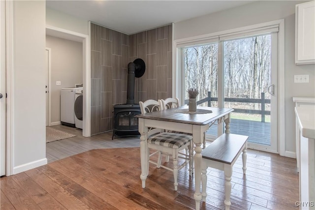 dining room with light wood-style flooring, washer / clothes dryer, a wood stove, and baseboards
