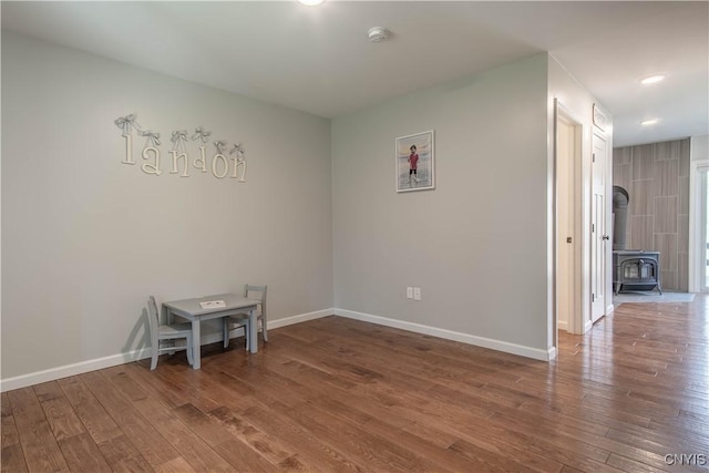 unfurnished room featuring a wood stove, recessed lighting, wood finished floors, and baseboards