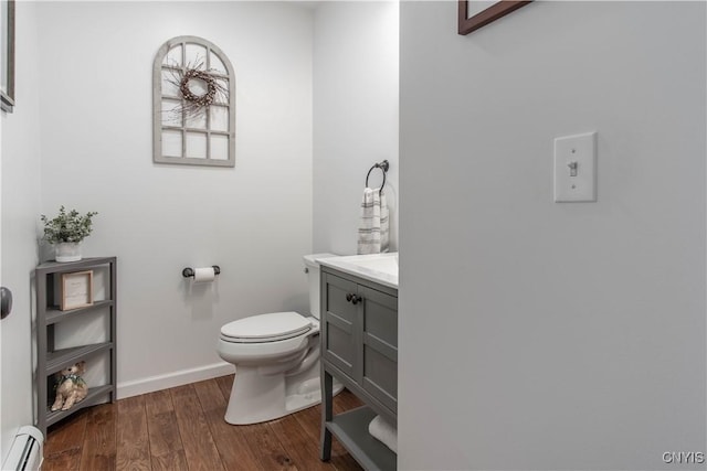 half bathroom featuring wood finished floors, a baseboard heating unit, toilet, vanity, and baseboards