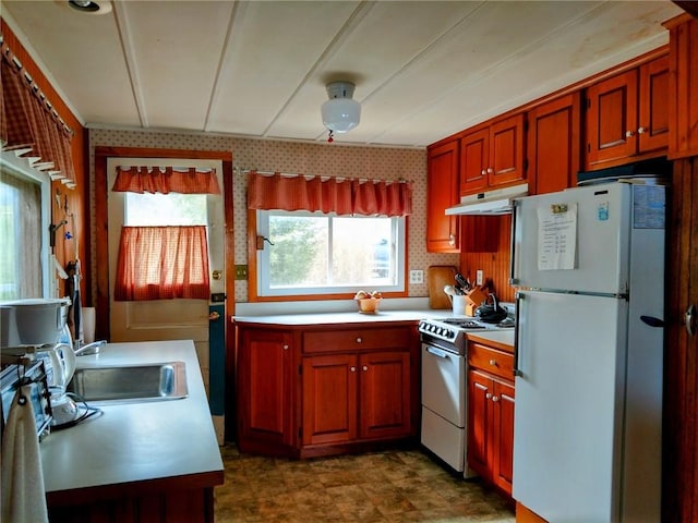 kitchen with freestanding refrigerator, a wealth of natural light, under cabinet range hood, gas stove, and a sink