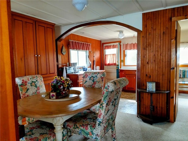 dining space featuring wood walls, arched walkways, and light colored carpet