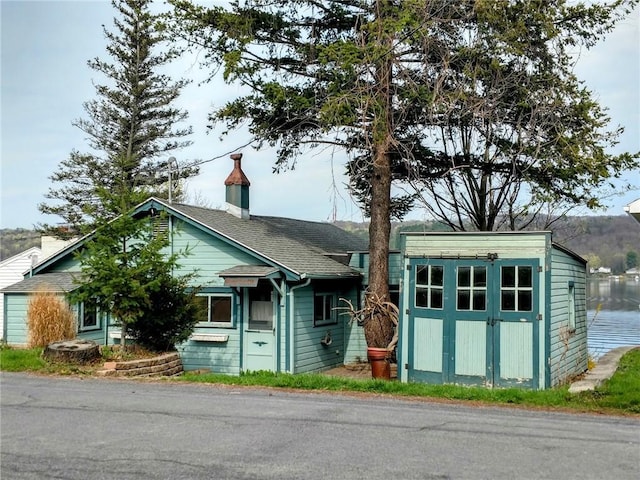 view of front of house with a storage unit, a chimney, roof with shingles, and an outbuilding