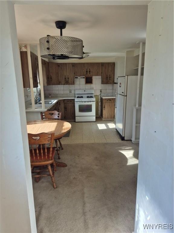 kitchen with brown cabinets, decorative backsplash, a sink, light countertops, and white appliances