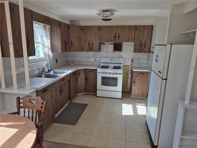 kitchen with white appliances, brown cabinetry, light countertops, backsplash, and a sink