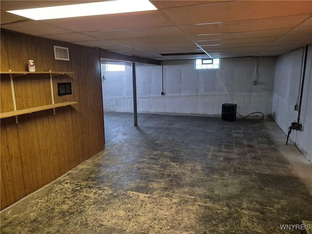 below grade area with a paneled ceiling, visible vents, and wood walls