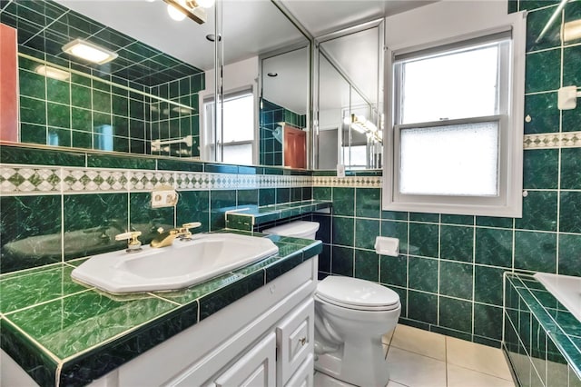 bathroom featuring a healthy amount of sunlight, toilet, tile patterned flooring, and tile walls
