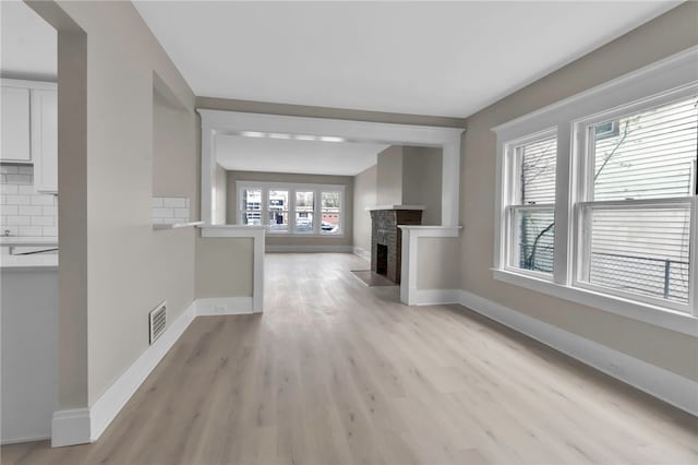 unfurnished living room with a fireplace with flush hearth, visible vents, baseboards, and light wood-style floors