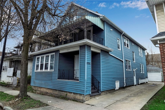view of side of property with an outdoor structure, a detached garage, and a balcony