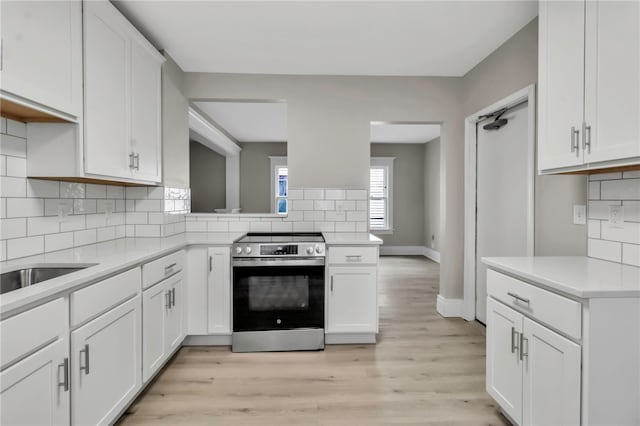 kitchen with decorative backsplash, light countertops, white cabinets, and stainless steel electric range