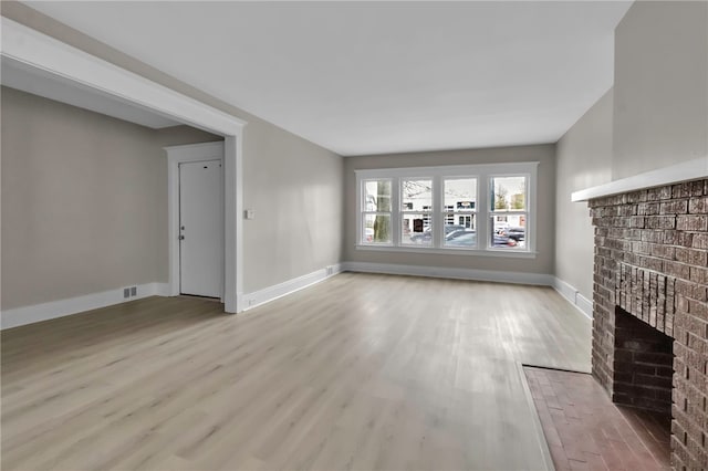 unfurnished living room with a brick fireplace, light wood finished floors, and baseboards