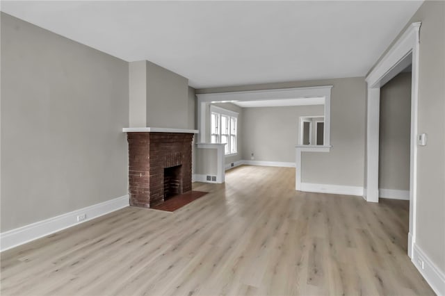 unfurnished living room with a brick fireplace, wood finished floors, and baseboards