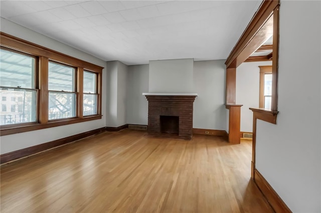 unfurnished living room with baseboards, visible vents, light wood-style floors, and a brick fireplace