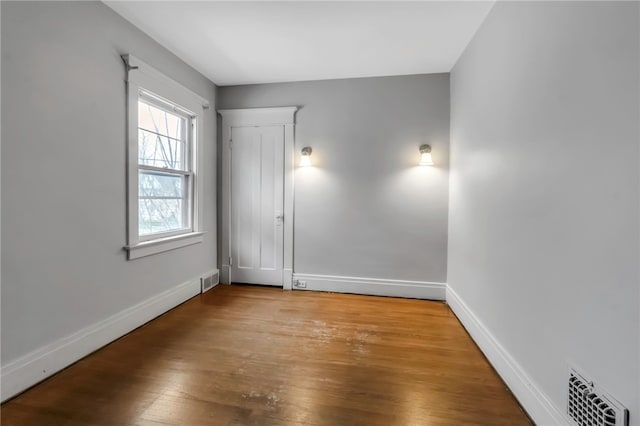 empty room with wood finished floors, visible vents, and baseboards