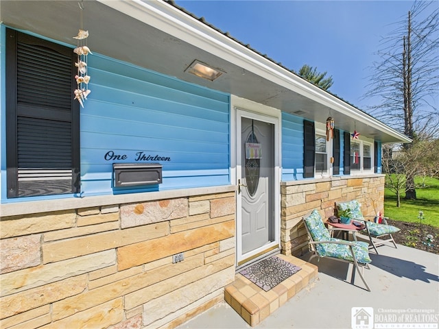 view of exterior entry featuring stone siding and covered porch
