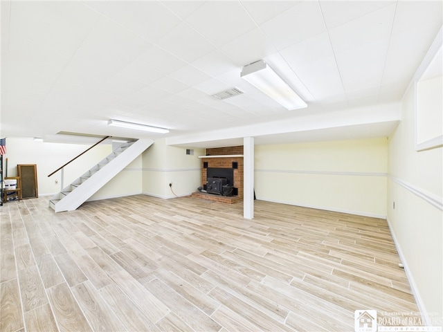 finished basement with a wood stove, light wood-type flooring, stairs, visible vents, and baseboards