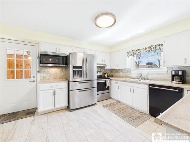 kitchen with stainless steel appliances, under cabinet range hood, white cabinets, backsplash, and a sink