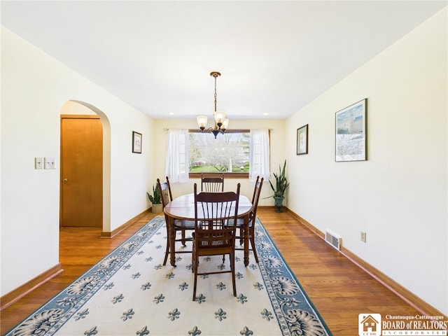dining area featuring arched walkways, wood finished floors, baseboards, visible vents, and a notable chandelier