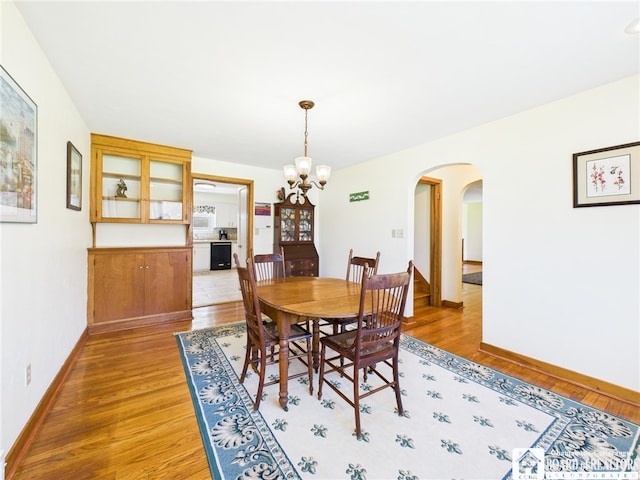 dining space featuring arched walkways, light wood-style flooring, a chandelier, and baseboards