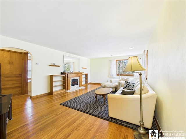 living area with arched walkways, a fireplace with flush hearth, wood finished floors, and baseboards