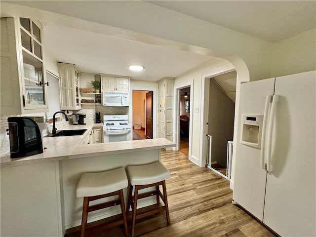kitchen featuring white appliances, light wood-style flooring, open shelves, light countertops, and a sink