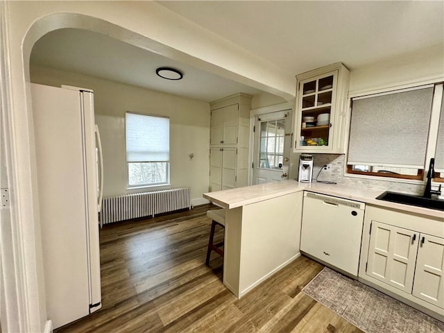 kitchen with radiator, a sink, a peninsula, white appliances, and dark wood finished floors